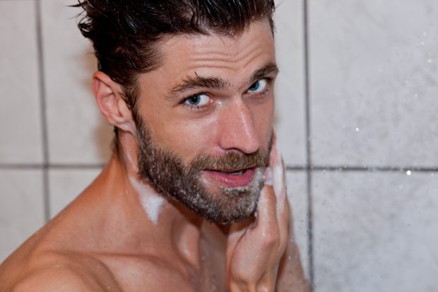 Un uomo di bell'aspetto si prende cura della propria barba lavandola con il sapone.